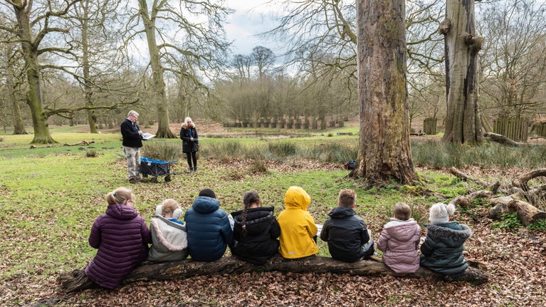 A group of schoolchildren sit on a log in a deer park at Dunham Massey